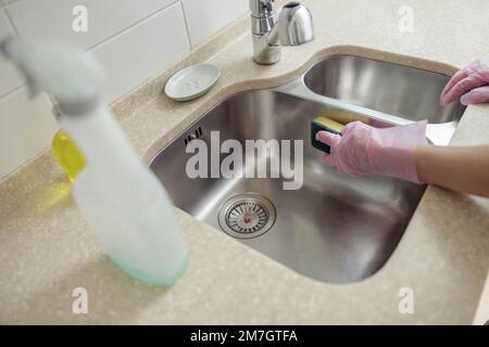 Gros plan de l'évier de nettoyage des mains de housemaid avec une éponge et un spray sur la cuisine maison Banque D'Images