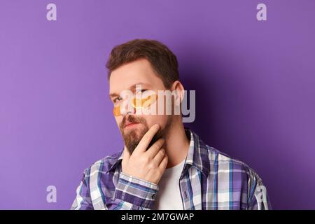 Homme en t-shirt blanc avec les taches oculaires se tiennent contre fond violet. Auto-soin de routine Banque D'Images