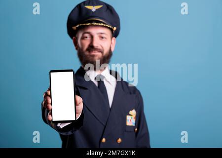 Avion capitan montrant smartphone avec écran blanc vierge gros plan, téléphone publicité produit maquette avec espace de copie. Avion pilote tenant un téléphone avec un écran vide pour les publicités promotionnelles de l'application Banque D'Images