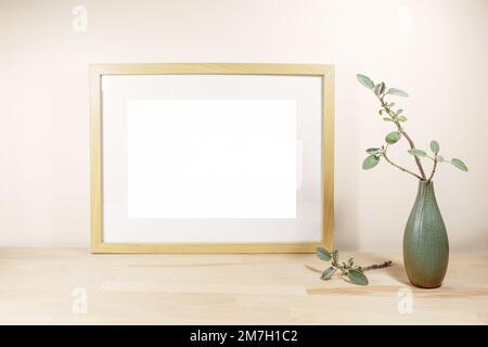 Cadre horizontal vide avec passe-partie comme maquette et un vase avec une branche de sauge sur une table ou un bureau en bois clair devant un mur beige, inter naturel Banque D'Images