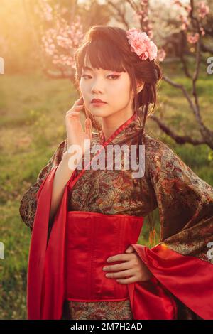 Portrait de style asiatique de la jeune femme en kimono séjour dans le jardin fleuri au coucher du soleil Banque D'Images