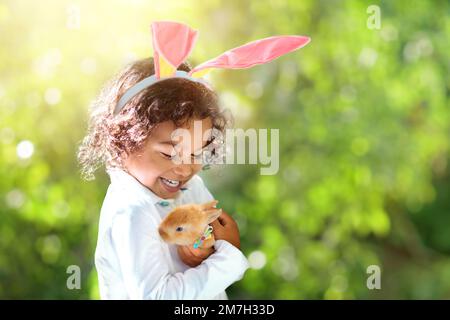 Petit garçon mausseux avec lapin de Pâques. Enfant jouant avec un animal de compagnie de lapin. Enfant dans les oreilles de lapin sur la chasse aux œufs de Pâques. Fête de printemps dans un jardin ensoleillé. Banque D'Images