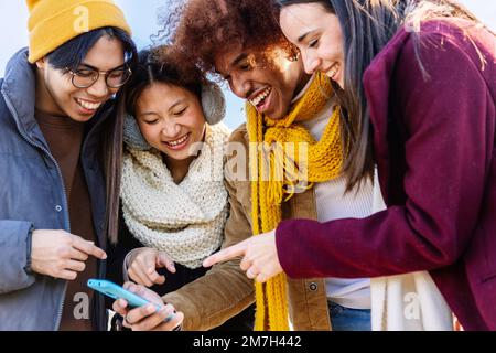 Des amis multiraciaux rient ensemble en regardant du contenu sur les réseaux sociaux sur leur téléphone Banque D'Images