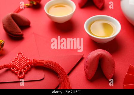 Biscuits fortune, enveloppe et tasses de thé sur fond rouge, gros plan. Célébration du nouvel an Banque D'Images