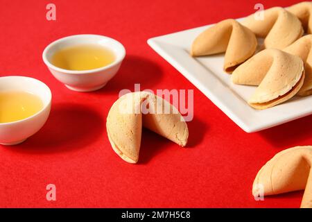 Assiette avec biscuits fortune et tasses de thé sur fond rouge. Célébration du nouvel an Banque D'Images