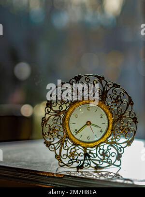 L'arrière-plan bokeh affiche l'horloge de bureau rétro sur une table blanche au premier plan. L'horloge est en métal d'or vintage avec un placarde décoratif sur un support en fil de fer. Banque D'Images