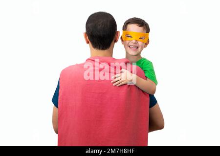 Mon adorable super père. Affectueux, un petit enfant câline le père avec amour, porte un masque orange, vêtu de costumes de super-héros, confiant dans la défense et le papa Banque D'Images