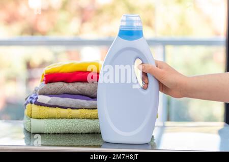 Prise de vue d'une femme tenant une bouteille de détergent et une pile de vêtements sur un lave-linge Banque D'Images