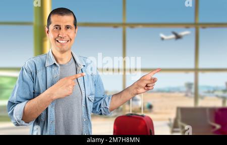 Homme se tenant souriant à l'aéroport et regardant la caméra pointant avec deux mains et des doigts sur le côté. Banque D'Images