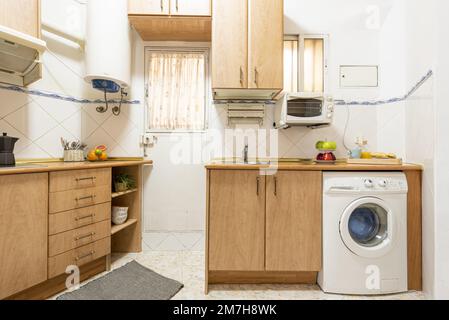 Cuisine traditionnelle avec armoires en bois clair avec appareils encastrés blancs, carrelage blanc, petites fenêtres et comptoir en merisier Banque D'Images