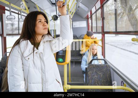 Portrait d'une jolie femme avec de longs cheveux foncés portant une robe blanche rêvant et pensant à des projets futurs. D'autres passagers assis au téléphone et regardant la vie en ville à travers les fenêtres de tram. Banque D'Images