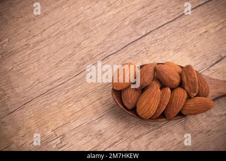 Amandes salées dans une cuillère en bois sur fond en bois Banque D'Images