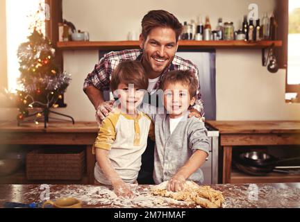 Une grande surprise pour les mamans. deux jeunes frères cuisant avec leur père dans la cuisine. Banque D'Images