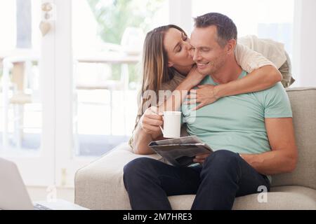 Obtenir sa dose quotidienne de café, de baisers et de nouvelles. un couple se détendant avec le café et le journal à la maison. Banque D'Images