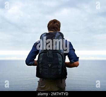 La vie d'un aventurier... vue arrière d'un jeune homme debout et regardant sur une étendue d'eau. Banque D'Images