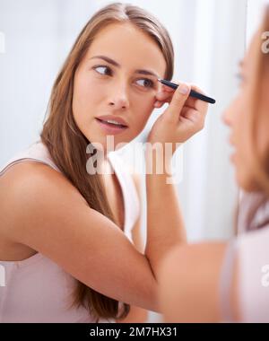 Créer la voûte plantaire parfaite. Une jeune femme en train de touiller ses sourcils devant un miroir. Banque D'Images