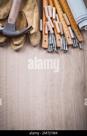 Les goujons de mesure en bois Blueprints une paire de gants de protection et des clous métalliques sur panneau de bois vue verticale concept de construction. Banque D'Images