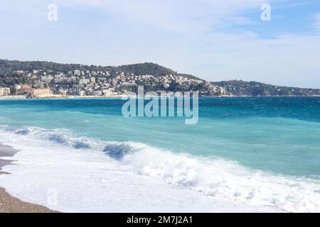 Les vagues se brisent dans la plage de sable avec la ville à flanc de colline en arrière-plan Banque D'Images