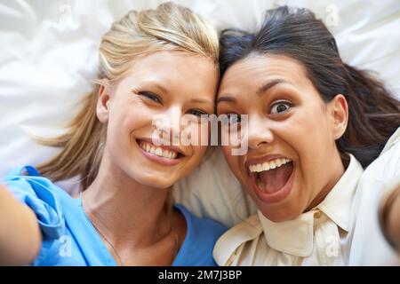 Je vous en réjouis. Portrait grand angle de deux jeunes femmes séduisantes prenant des selfies tout en étant allongé sur un lit. Banque D'Images