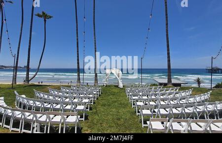 Une vue panoramique de chaises blanches dans une rangée sur l'herbe verte prête pour une cérémonie de mariage sur la plage Banque D'Images