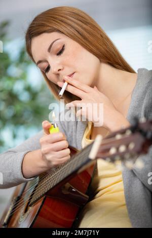 femme fumant une cigarrete tout en jouant de la guitare Banque D'Images
