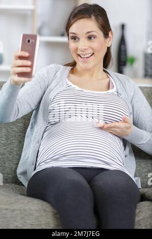 jeune femme enceinte assise sur un canapé et prenant une photo de selfie Banque D'Images