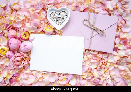 Fond de rose bourgeons et pétales avec enveloppe et carte vierge au centre et plaque en céramique avec coeur en bois. Pose à plat, vue de dessus. De la mère Banque D'Images