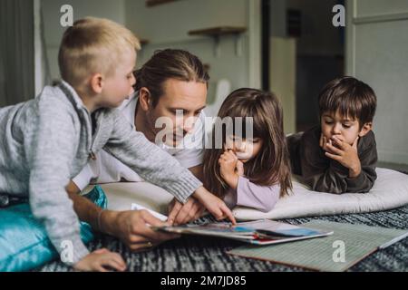 Un travailleur de la garde d'enfants de sexe masculin lit un livre d'histoire aux élèves de la maternelle Banque D'Images