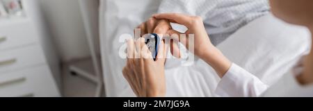 Vue rognée d'un médecin brouillé portant un oxymètre de pouls sur le doigt d'un patient âgé à l'hôpital, bannière, image de stock Banque D'Images