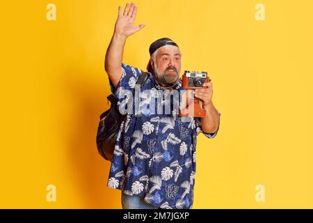 Portrait d'un homme mûr et gras dans une chemise élégante posant, prenant des photos avec un appareil photo vintage sur fond jaune vif de studio Banque D'Images