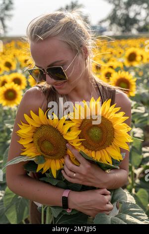 Belle femme dans le champ de tournesol au coucher du soleil appréciant la nature d'été. Blond attrayant avec de longs cheveux sains. Banque D'Images