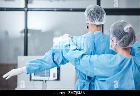 Médecin, uniforme et chirurgien se préparer à la chirurgie, à l'opération ou aux soins médicaux. Infirmière aidant le travailleur à porter des vêtements de sécurité en cas d'utilisation d'urgence Banque D'Images