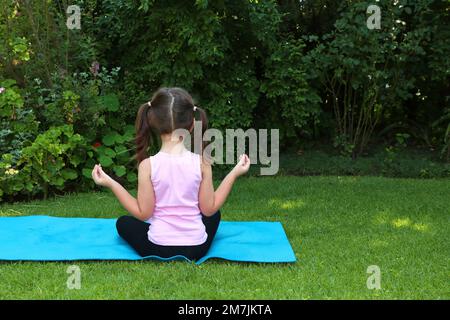 Une jeune fille de 7-10 ans faisant du yoga pose dans le jardin portant des picots sur un tapis de yoga bleu Banque D'Images