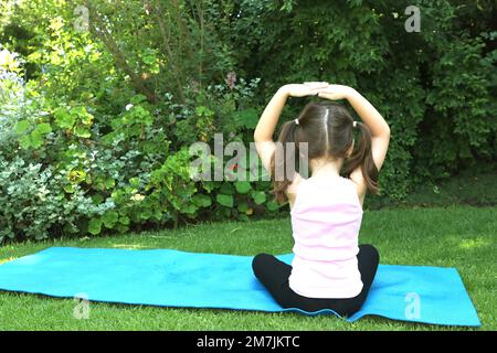 Une jeune fille de 7-10 ans faisant du yoga pose dans le jardin portant des picots sur un tapis de yoga bleu Banque D'Images