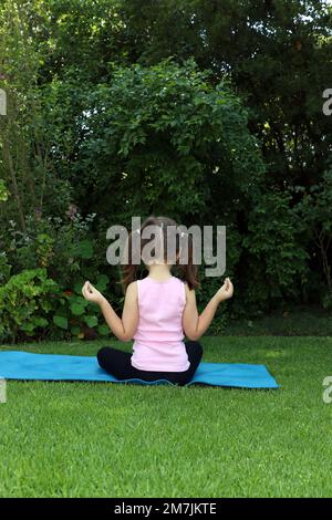 Une jeune fille de 7-10 ans faisant du yoga pose dans le jardin portant des picots sur un tapis de yoga bleu Banque D'Images