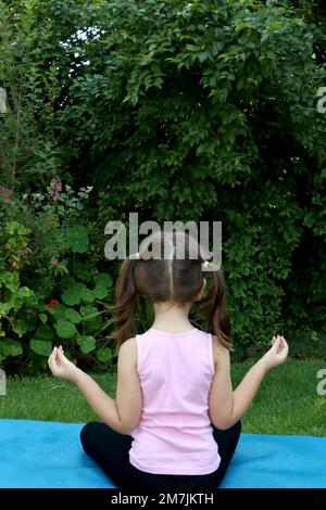 Une jeune fille de 7-10 ans faisant du yoga pose dans le jardin portant des picots sur un tapis de yoga bleu Banque D'Images