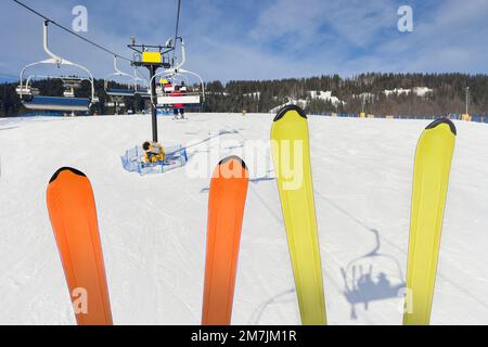 les skieurs s'assoient sur la remontée mécanique et montrent leurs skis. ski sur fond de paysage d'hiver de la station de ski. Banque D'Images