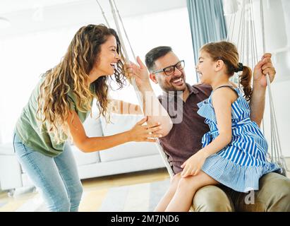 enfant fille famille heureuse mère père canapé jouer amusant ensemble fille souriante maison balançoire intérieure Banque D'Images