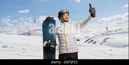 Homme avec un snowboard prenant un selfie avec un smartphone sur une montagne enneigée Banque D'Images