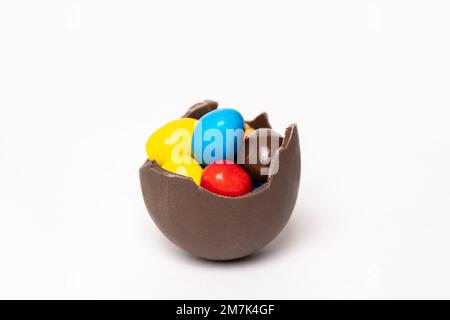 Œuf de pâques au chocolat craqué avec de petites friandises rondes colorées sur fond blanc, espace pour les copies, vue latérale. Chocolat pour les enfants. Concept de Pâques. Banque D'Images