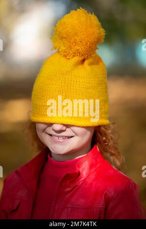 La petite fille a tiré un chapeau tricoté jaune sur ses yeux. La chute est arrivée. Banque D'Images