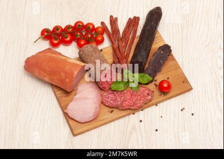 Différents types de saucisses jambon, mahan, salami sur une planche en bois décorée de tomates et de basilic Banque D'Images