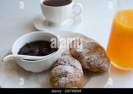 Croissant frais sur une assiette blanche, présentation avec confiture de fraises, jus d'orange et thé. Banque D'Images