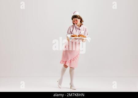 Belle jeune fille à l'image d'un serveur de restauration rétro portant 70s, 80s style de mode uniforme isolé sur fond de studio léger. Charme, publicité, ventes Banque D'Images