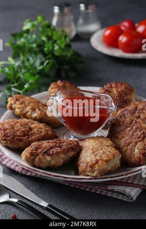 Côtelettes de filet de dinde et de flocons d'avoine, frites dans une casserole, servies avec de la sauce tomate sur une table grise Banque D'Images