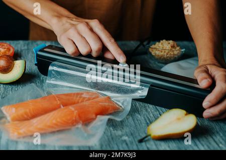 un jeune homme envide deux morceaux de saumon dans un sac à vide, à une table grise rustique Banque D'Images