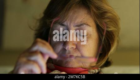 Portrait en gros plan d'une femme plus âgée mettant des lunettes de lecture regardant l'écran. Femme aînée dans sa lecture de 60s Banque D'Images