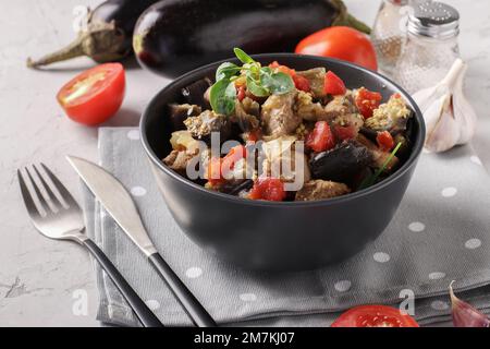 Ragoût de viande avec aubergines et tomates servi dans un bol sombre sur fond gris Banque D'Images