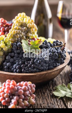 Des petits pains juteux de raisins dans un bol en bois, du vin rouge en arrière-plan. Banque D'Images