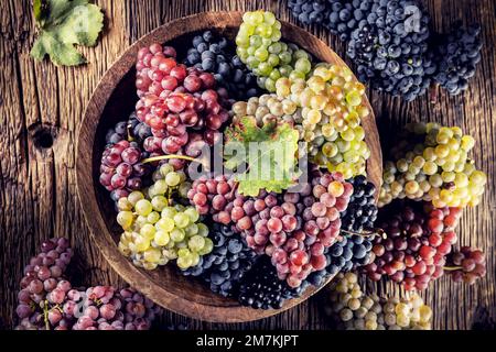 Des petits pains juteux de raisins dans un bol en bois, du vin rouge en arrière-plan. Banque D'Images